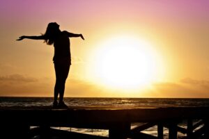 Frau steht am Meer vor der untergehenden Sonne